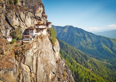 Das Tigers Nest schmiegt sich an den steilen Felsabhang vor einer offenen Berglandschaft